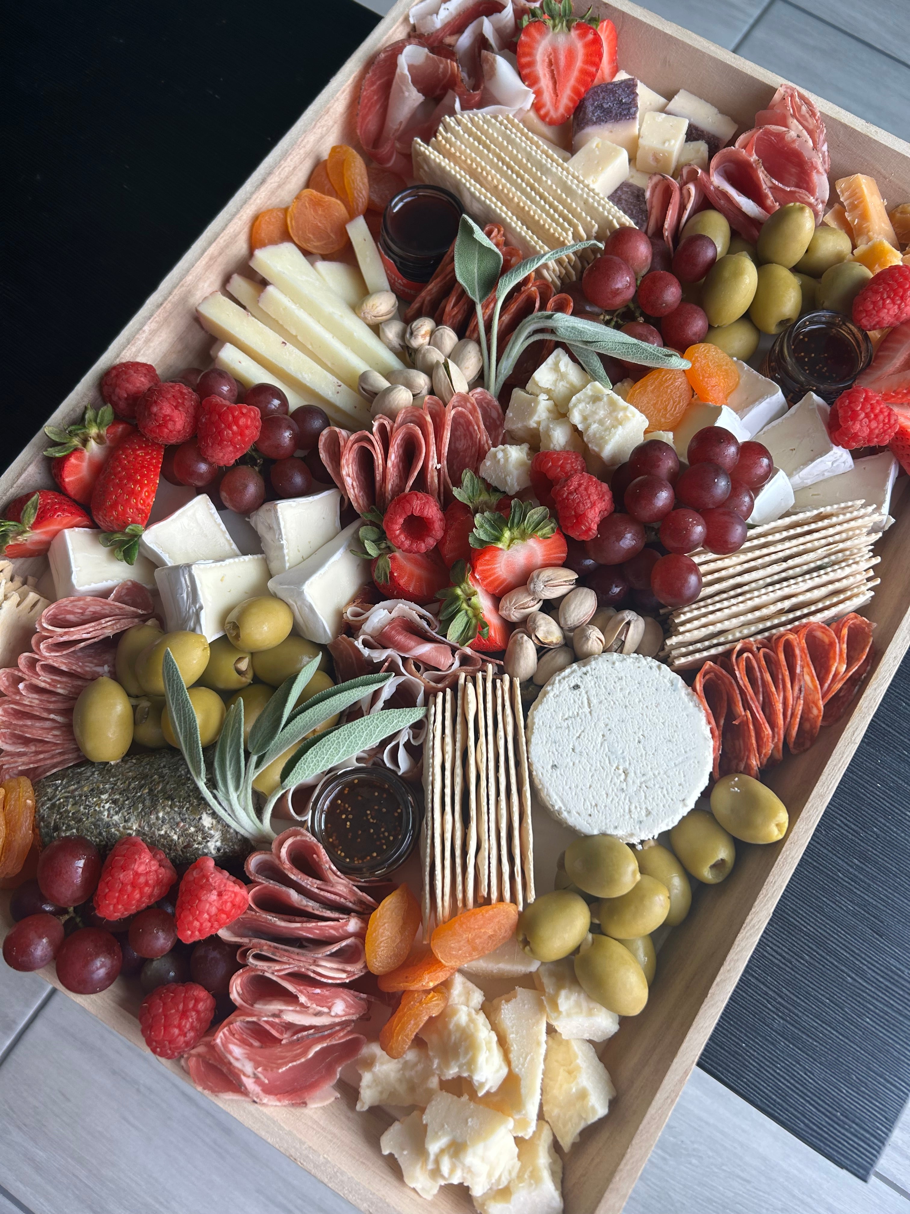 Assorted charcuterie board with meats, cheeses, fruits, and vegetables on a disposable wooden board.
